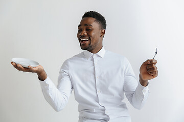 Image showing Young smiling attractive african american guy holding empty dish and spoon isolated on grey background. Copy space and mock up. Blank template background.