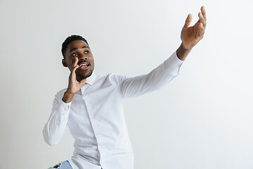 Image showing Handsome Afro American man in classic shirt is smiling, looking at camera and pointing away, against white brick wall