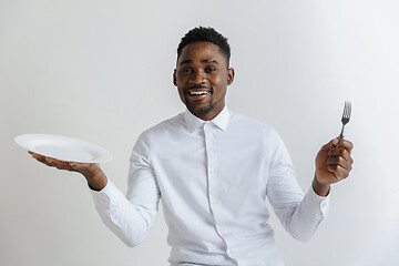 Image showing Young smiling attractive african american guy holding empty dish and fork isolated on grey background. Copy space and mock up. Blank template background.