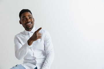 Image showing Handsome Afro American man in classic shirt is smiling, looking at camera and pointing away, against white brick wall