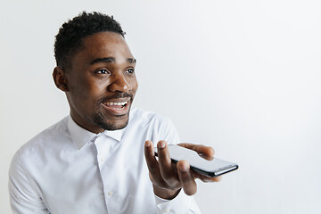 Image showing Indoor portrait of attractive young black african man isolated on gray background, holding blank smartphone, using voice control, feeling happy and surprised. Human emotions, facial expression concep