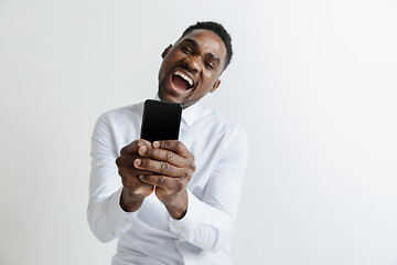 Image showing Indoor portrait of attractive young black african man isolated on pink background, holding blank smartphone, smiling at camera, showing screen, feeling happy and surprised. Human emotions, facial