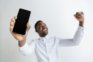 Image showing Indoor portrait of attractive young black african man isolated on pink background, holding blank smartphone, smiling at camera, showing screen, feeling happy and surprised. Human emotions, facial