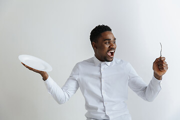 Image showing Young happy african american guy holding empty dish and fork isolated on grey background. Copy space and mock up. Blank template background.