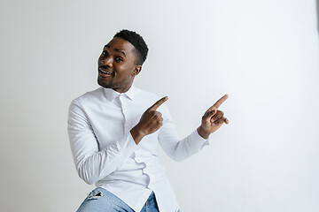 Image showing Handsome Afro American man in classic shirt is smiling, looking at camera and pointing away, against white brick wall