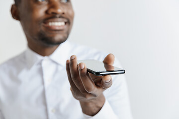 Image showing Indoor portrait of attractive young black african man isolated on gray background, holding blank smartphone, using voice control, feeling happy and surprised. Human emotions, facial expression concep