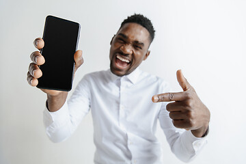 Image showing Indoor portrait of attractive young black african man isolated on pink background, holding blank smartphone, smiling at camera, showing screen, feeling happy and surprised. Human emotions, facial