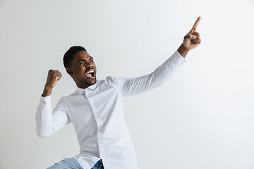 Image showing Handsome Afro American man in classic shirt is smiling, looking at camera and pointing away, against white brick wall