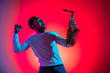 Image showing African American handsome jazz musician interacts with audience and holding the saxophone.