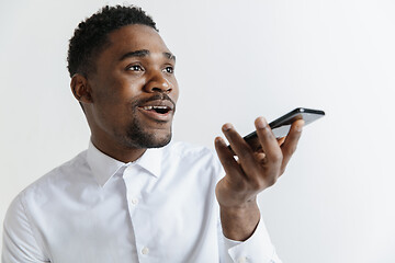 Image showing Indoor portrait of attractive young black african man isolated on gray background, holding blank smartphone, using voice control, feeling happy and surprised. Human emotions, facial expression concep