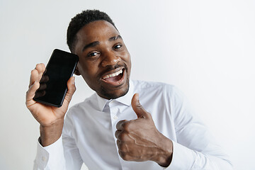 Image showing Indoor portrait of attractive young black african man isolated on pink background, holding blank smartphone, smiling at camera, showing screen, feeling happy and surprised. Human emotions, facial