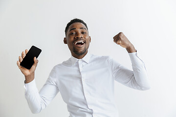 Image showing Indoor portrait of attractive young black african man isolated on pink background, holding blank smartphone, smiling at camera, showing screen, feeling happy and surprised. Human emotions, facial