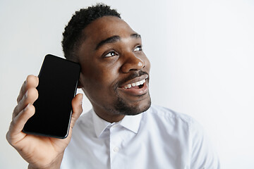 Image showing Indoor portrait of attractive young black african man isolated on pink background, holding blank smartphone, smiling at camera, showing screen, feeling happy and surprised. Human emotions, facial