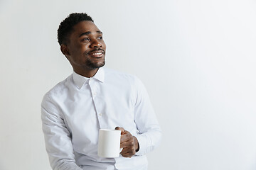 Image showing Coffee makes his day. Young handsome African man drinking coffee and looking away while sitting at his working place