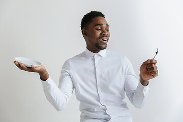 Image showing Young smiling attractive african american guy holding empty dish and spoon isolated on grey background. Copy space and mock up. Blank template background.