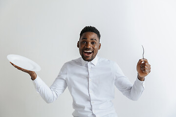 Image showing Young happy african american guy holding empty dish and fork isolated on grey background. Copy space and mock up. Blank template background.