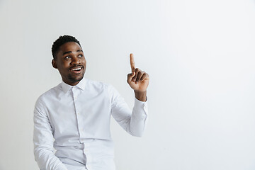 Image showing Handsome Afro American man in classic shirt is smiling, looking at camera and pointing away, against white brick wall