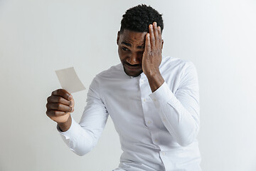 Image showing Young afro man with a disappointed unhappy sad expression lost a bet on gray studio background. Human facial emotions and betting concept.