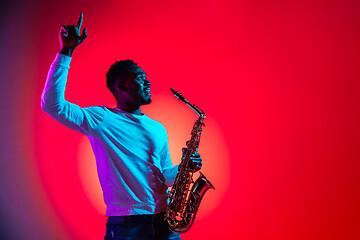 Image showing African American handsome jazz musician interacts with audience and holding the saxophone.
