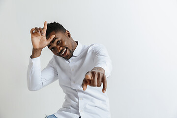 Image showing Losers go home. Portrait of happy guy showing loser sign over forehead and smiling in cause of victory and laughing over gray background