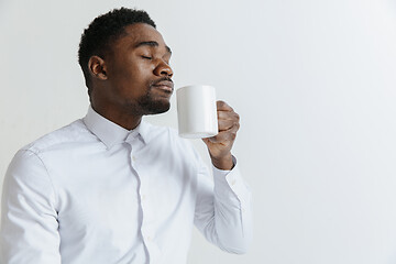 Image showing Coffee makes his day. Young handsome African man drinking coffee and looking away while sitting at his working place