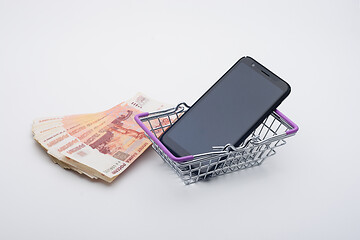 Image showing Next to a stack of five thousandth bills is a grocery basket with a cell phone