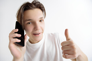 Image showing Young handsome teenager showing smartphone screen and signing OK isolated on gray background