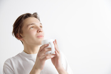 Image showing Taking a coffee break. Handsome young man holding coffee cup, smiling while standing against gray background