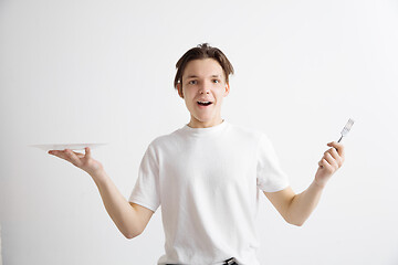 Image showing Young smiling attractive guy holding empty dish and fork isolated on grey background.