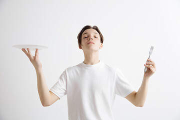 Image showing Young smiling attractive guy holding empty dish and fork isolated on grey background.