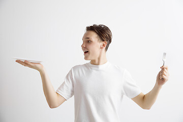 Image showing Young smiling attractive guy holding empty dish and fork isolated on grey background.