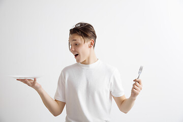 Image showing Young smiling attractive guy holding empty dish and fork isolated on grey background.