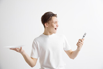 Image showing Young smiling attractive guy holding empty dish and fork isolated on grey background.