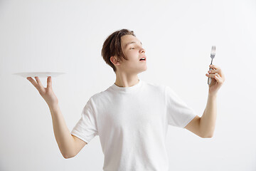 Image showing Young smiling attractive guy holding empty dish and fork isolated on grey background.