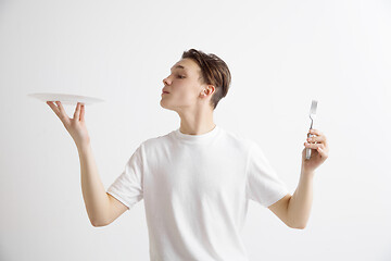 Image showing Young smiling attractive guy holding empty dish and fork isolated on grey background.