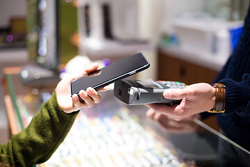 Image showing Woman paying with NFC technology on smart phone at shop