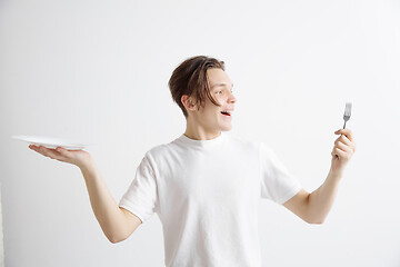 Image showing Young smiling attractive guy holding empty dish and fork isolated on grey background.