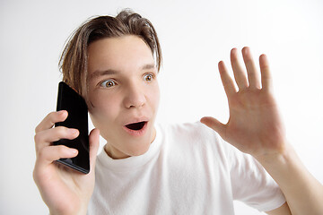 Image showing Young handsome teenager showing smartphone screen isolated on gray background in shock with a surprise face