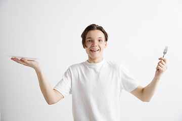 Image showing Young smiling attractive guy holding empty dish and fork isolated on grey background.