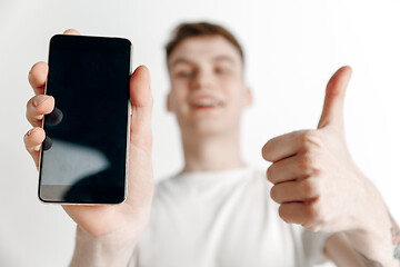 Image showing Young handsome man showing smartphone screen and signing OK isolated on gray background