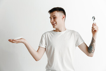 Image showing Young smiling attractive guy holding empty dish and fork isolated on grey background.