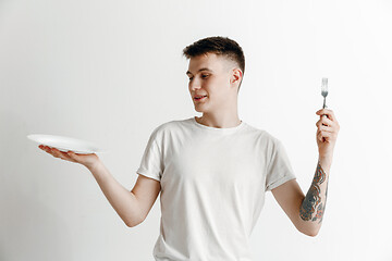 Image showing Young smiling attractive guy holding empty dish and fork isolated on grey background.