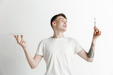 Image showing Young smiling attractive guy holding empty dish and fork isolated on grey background.