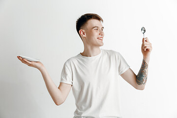 Image showing Young smiling attractive guy holding empty dish and fork isolated on grey background.