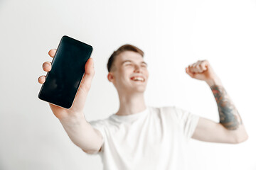 Image showing Young handsome man showing smartphone screen and signing OK isolated on gray background