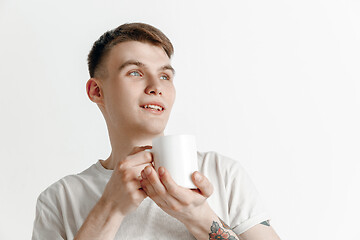 Image showing Taking a coffee break. Handsome young man holding coffee cup, smiling while standing against gray background