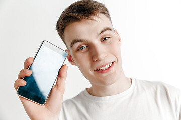 Image showing Young handsome man showing smartphone screen and signing OK isolated on gray background