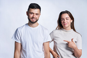 Image showing Smiling couple standing over light background, joyful female pointing at guy and winking