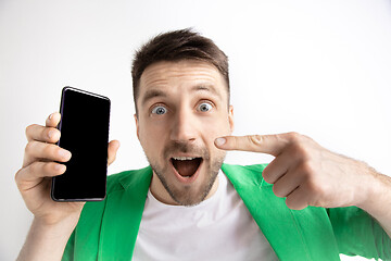 Image showing Young handsome man showing smartphone screen and signing OK isolated on gray background