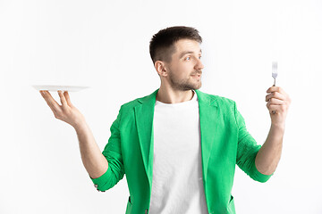 Image showing Young smiling attractive guy holding empty dish and fork isolated on grey background.